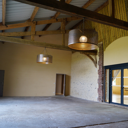 Intérieur spacieux rustique avec poutres en bois, lampes suspendues et sol en béton.