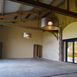 Intérieur spacieux rustique avec poutres en bois, lampes suspendues et sol en béton.