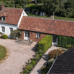 Vue aérienne d'une maison avec un toit en tuiles rouges, un jardin vert et une allée en gravier.