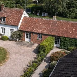 Vue aérienne d'une maison avec un toit en tuiles rouges, un jardin vert et une allée en gravier.
