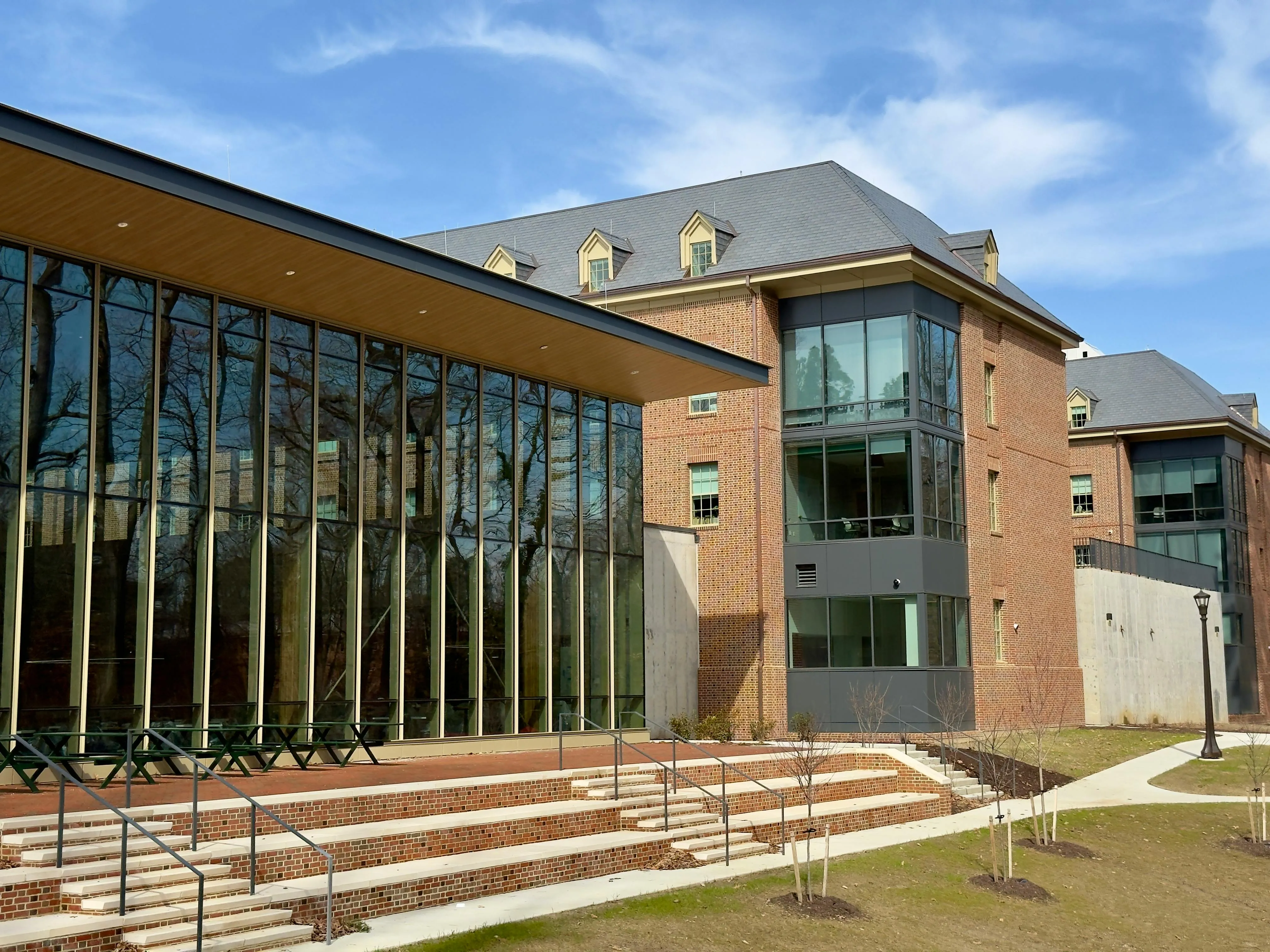 Modern brick and glass building with large windows, outdoor steps, and young trees under a blue sky.