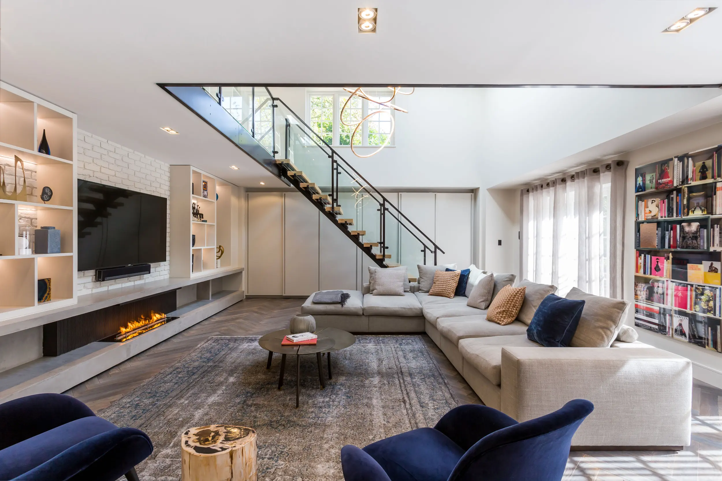 Modern three-sided bioethanol media wall fireplace with ribbed metal back panel, microcement base, bespoke joinery and integrated television. Angled view