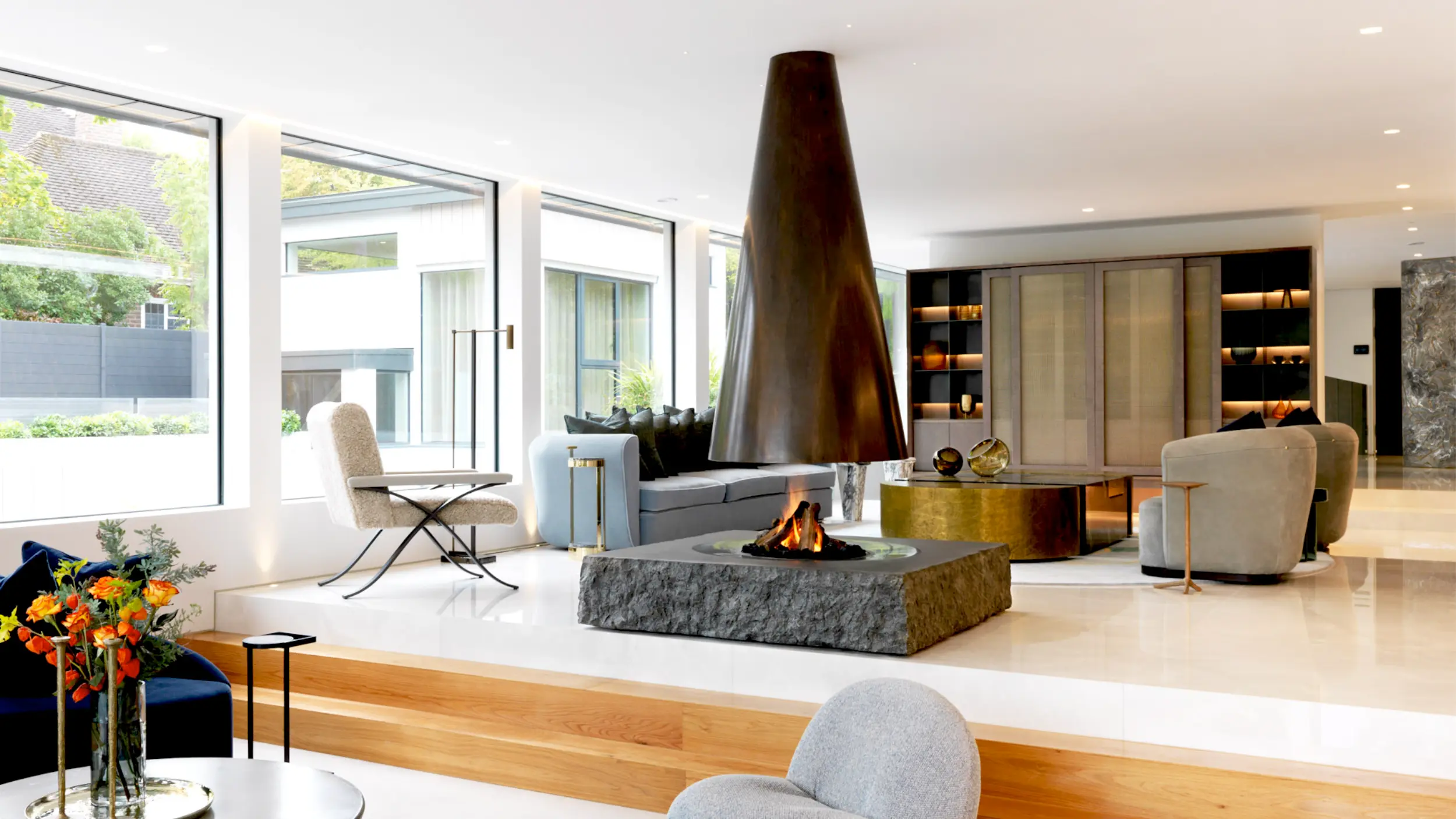 Suspended conical fireplace with antique brass canopy and carved hammered granite base as sculptural centrepiece in