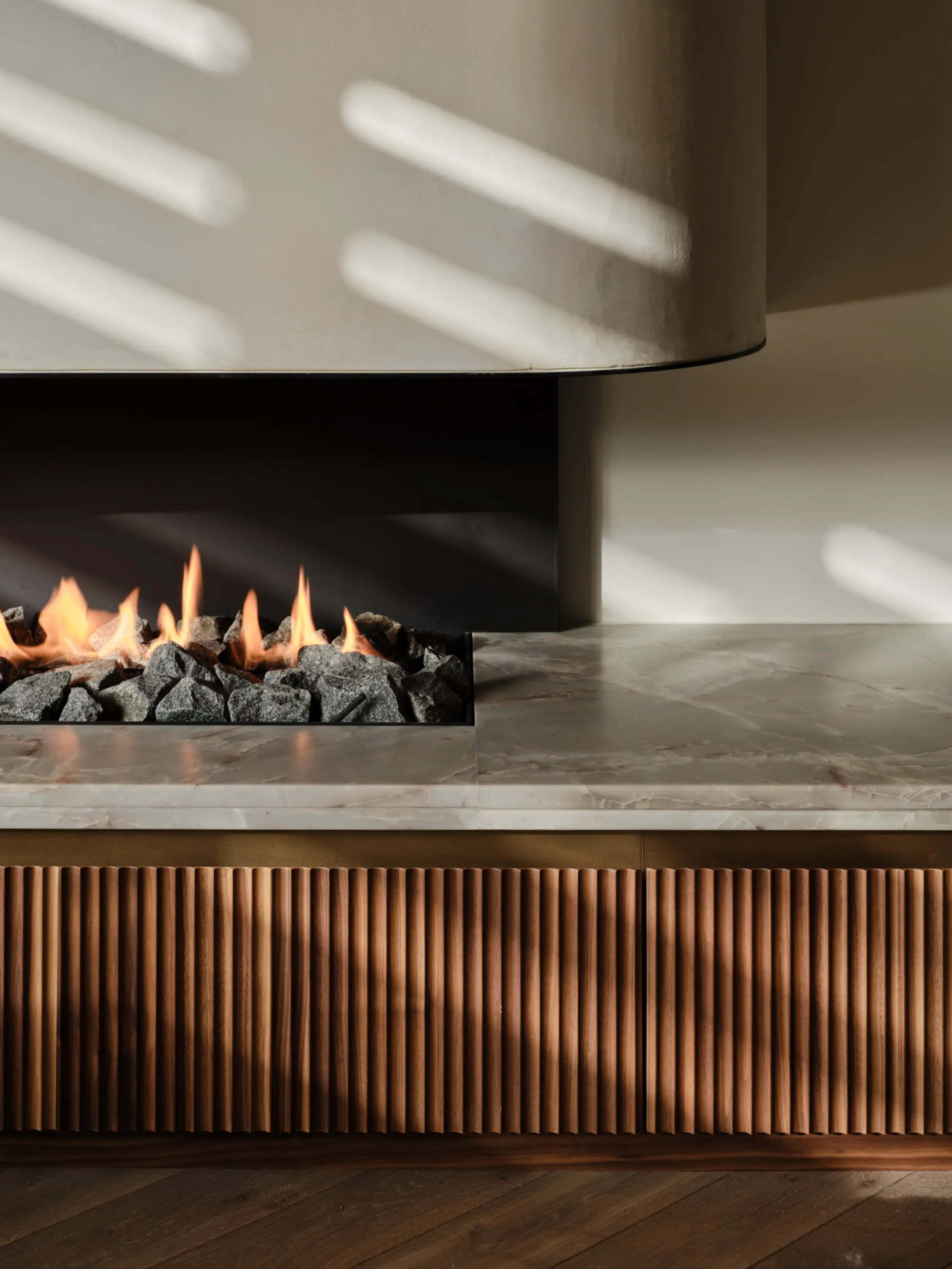 Detail view of the linear gas fireplace with fluted oak and stone, showing three-sided, open fireplace