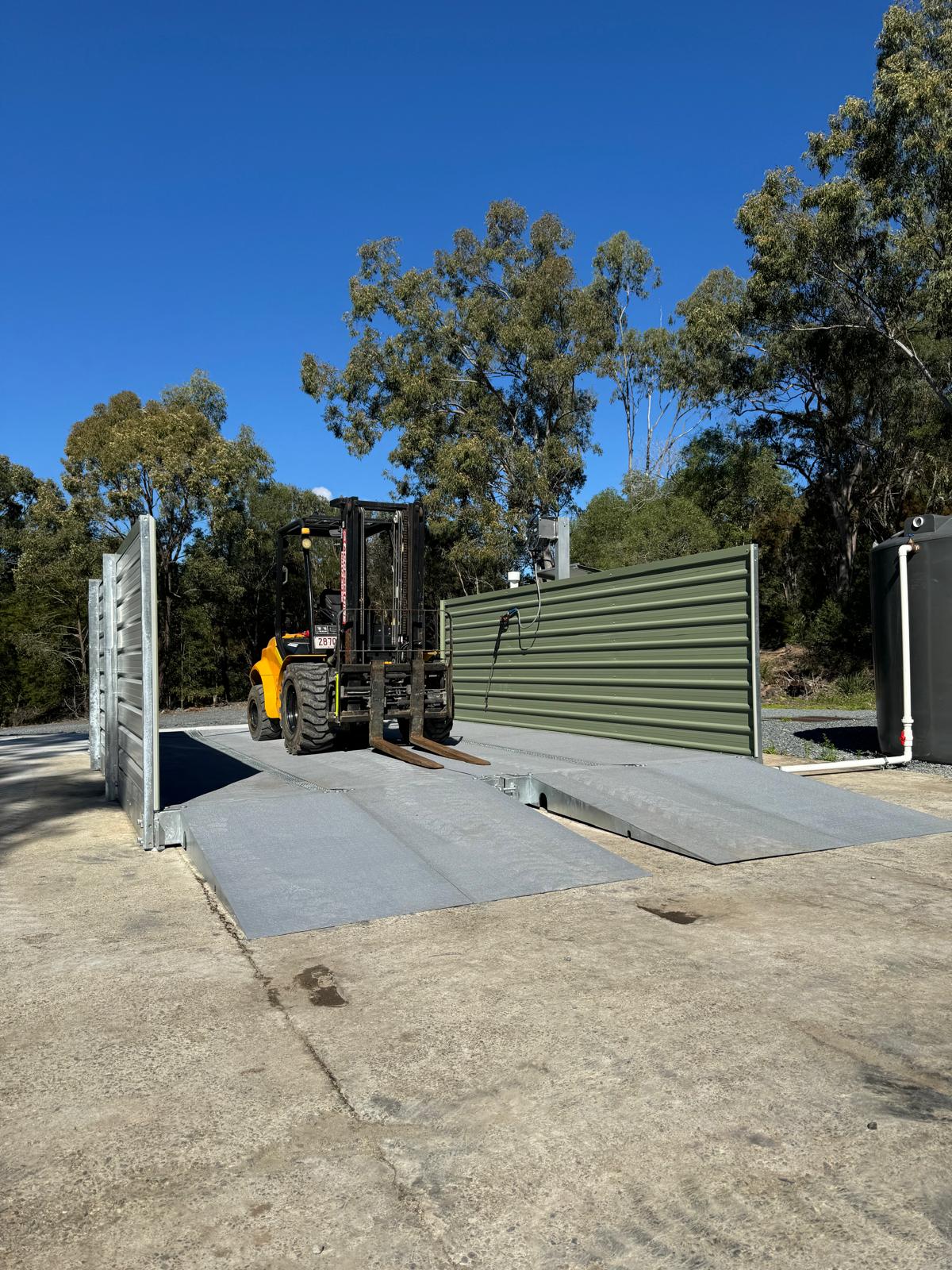 Forklift positioned in drive-through washdown bay with side screens and ramps