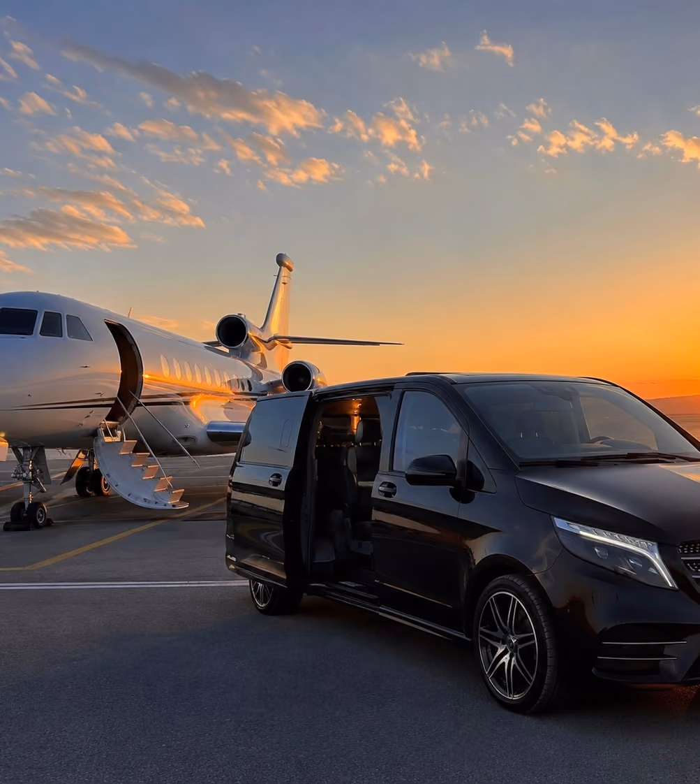 Private jet with stairs down and black van with open door parked on tarmac during sunset.