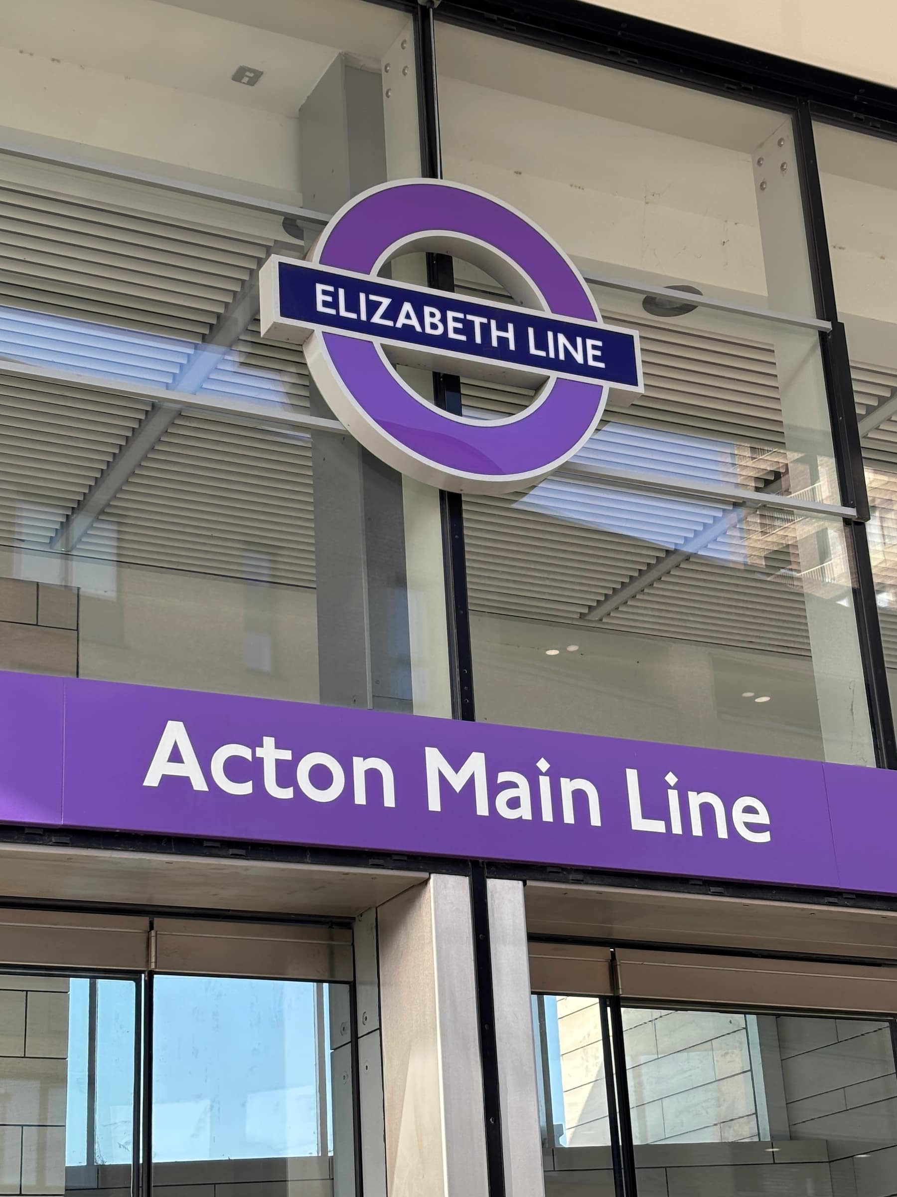 Purple sign reading Elizabeth Line and Acton Main Line at a train station entrance.
