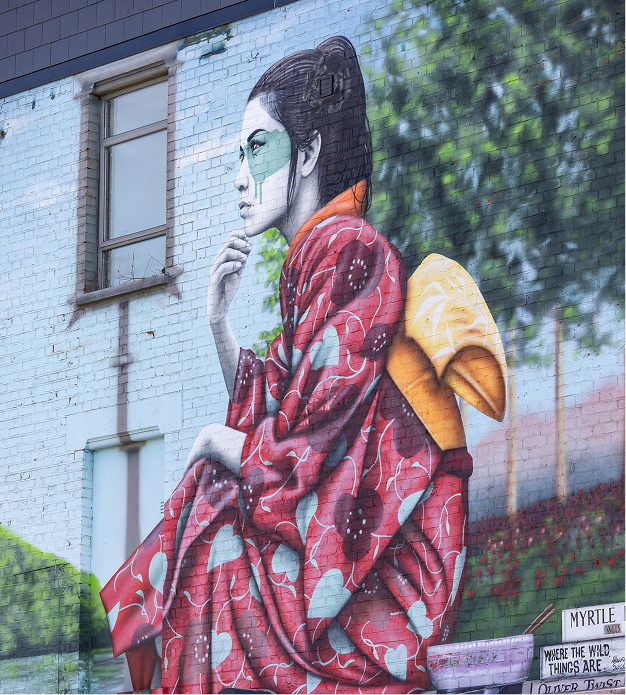 Mural of a woman in a red floral kimono with green paint on her face sitting on a wall with trees in background.