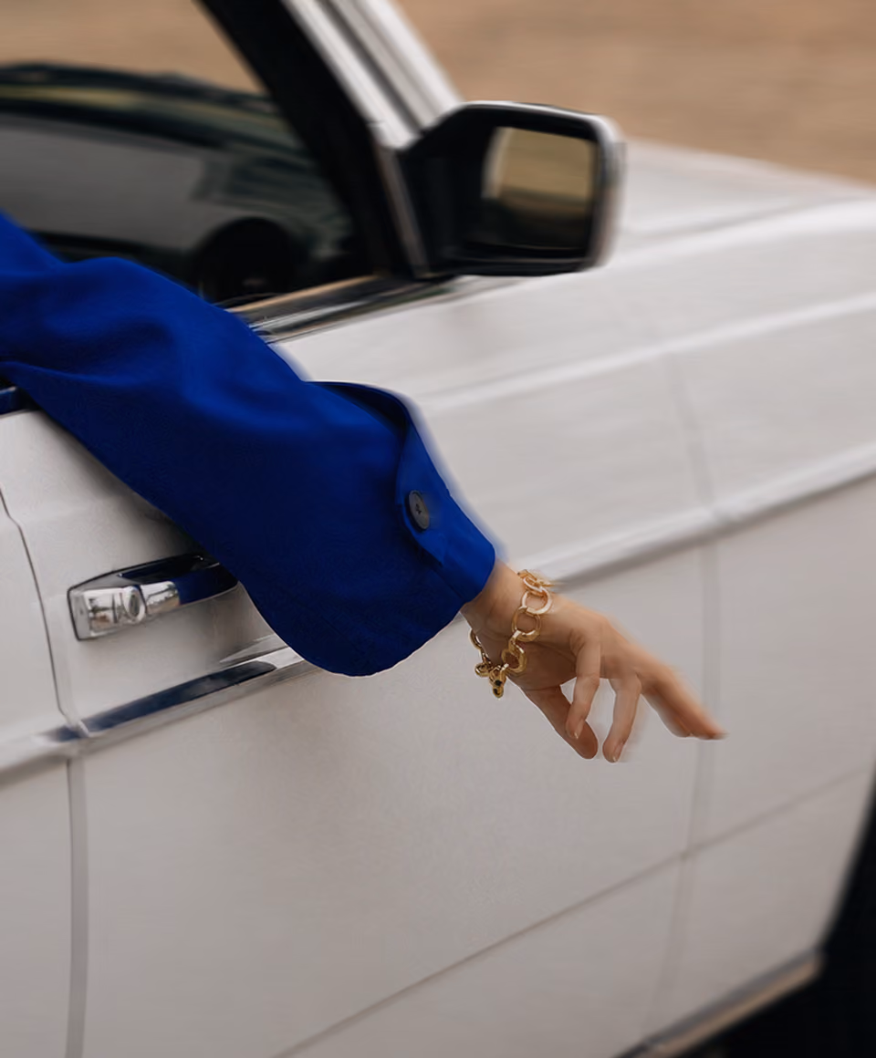 Person wearing a blue sleeve bracelet extending hand out of a white car window.