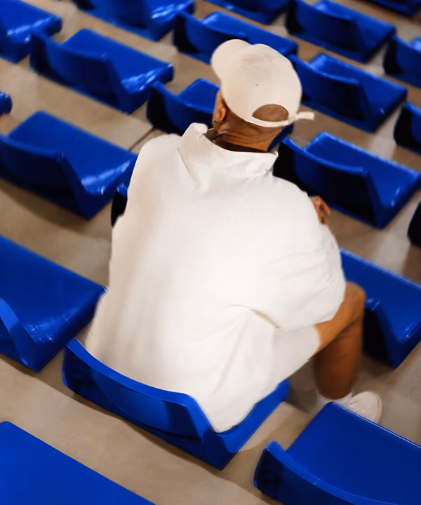 Person in white hoodie and cap sitting alone on blue stadium seats.