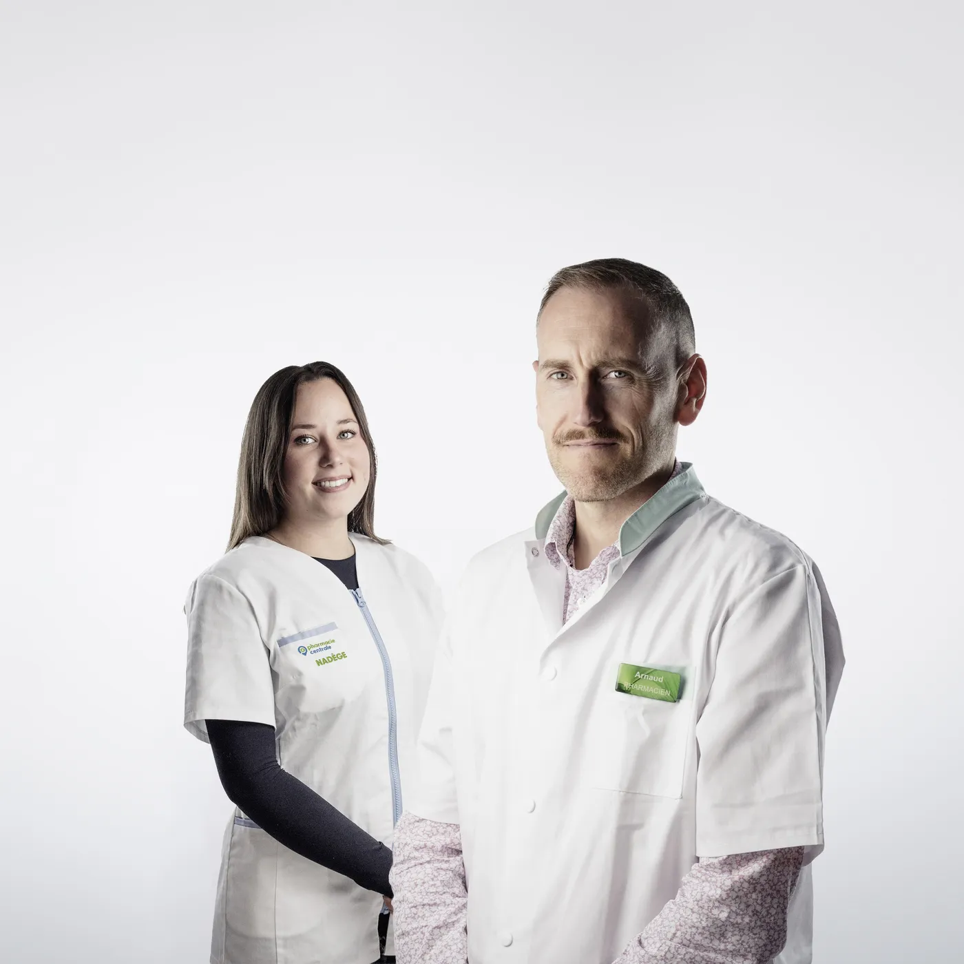 Deux professionnels de santé souriants en blouses blanches, fond blanc neutre.