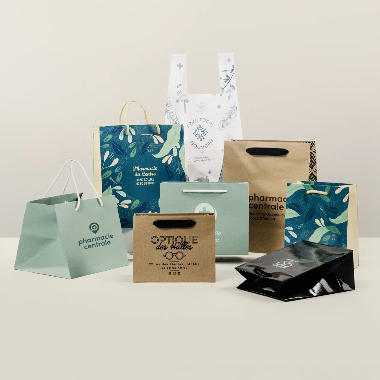 Huit sacs papier et plastique de pharmacie avec logos et motifs dans différentes couleurs posés sur une surface.