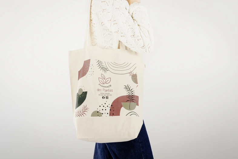 Personne portant un sac en tissu avec un design abstrait et message Pharmacie des Plantes.