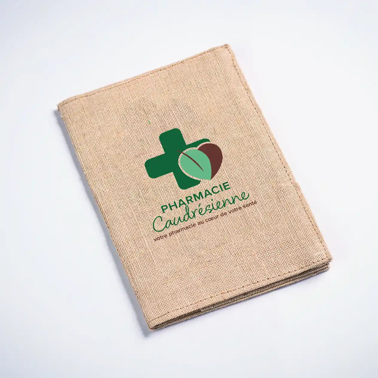 Étui beige en toile avec logo vert croix et feuille, texte "Pharmacie Caudrésienne" imprimé dessus.