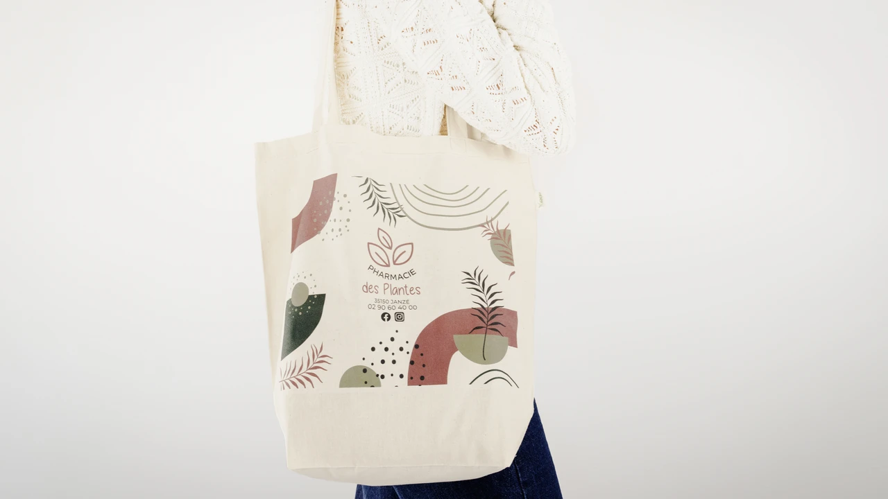 Personne portant un sac en toile avec un logo et des motifs abstraits verts et rouges.