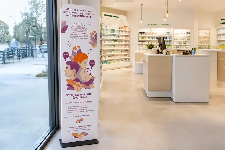 Totem informatif sur le mélanome en pharmacie moderne avec comptoir et étagères de médicaments.