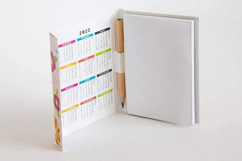 Carnet blanc ouvert avec un calendrier 2022 coloré et un crayon en bois inséré.
