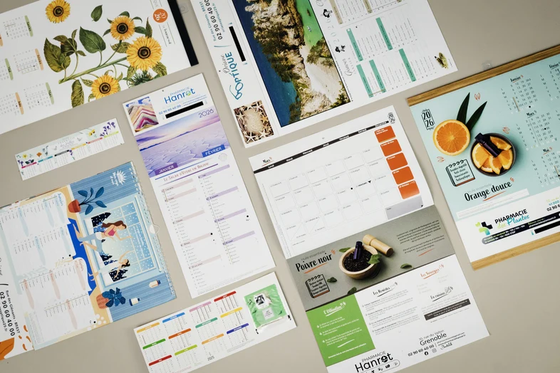 Calendriers personnalisés variés avec illustrations de fleurs, paysage, épices et oranges, posés sur une surface claire.