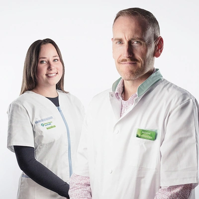 Deux professionnels de santé souriants en blouse blanche sur fond clair.