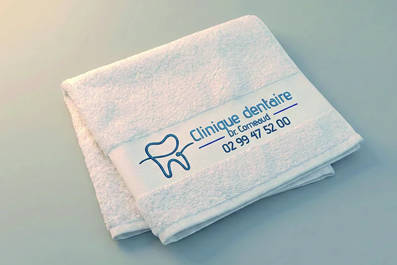 Serviette blanche pliée avec logo dentiste Clinique dentaire Dr. Corneaud et numéro de téléphone.