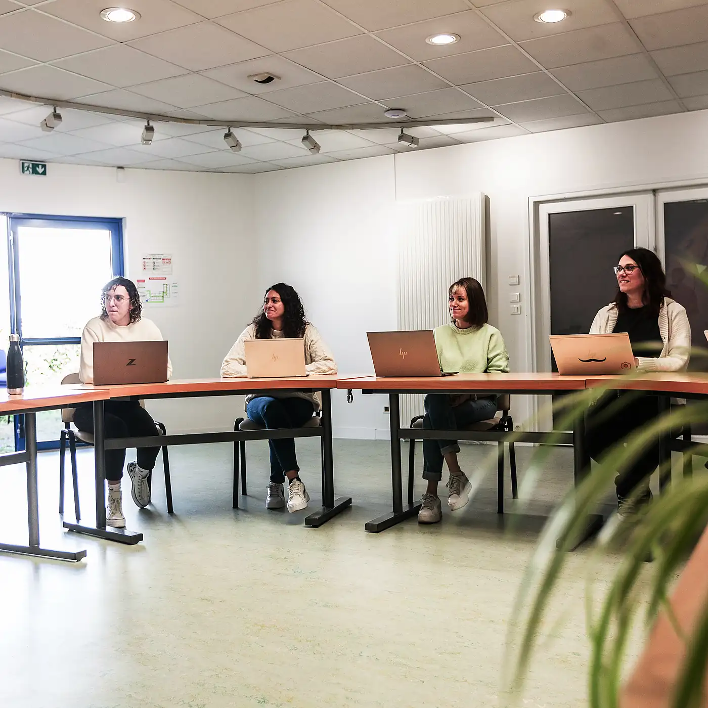 Quatre femmes assises en face à face avec des ordinateurs portables en réunion dans une salle claire.