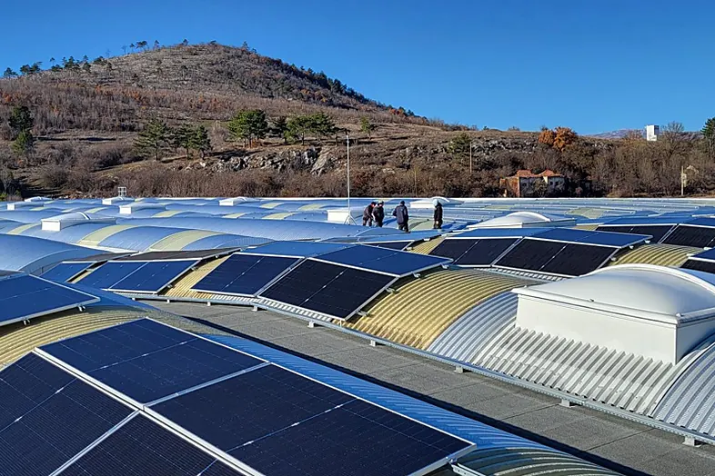 Panneaux solaires installés sur un toit ondulé avec des personnes travaillant et une colline en arrière-plan.