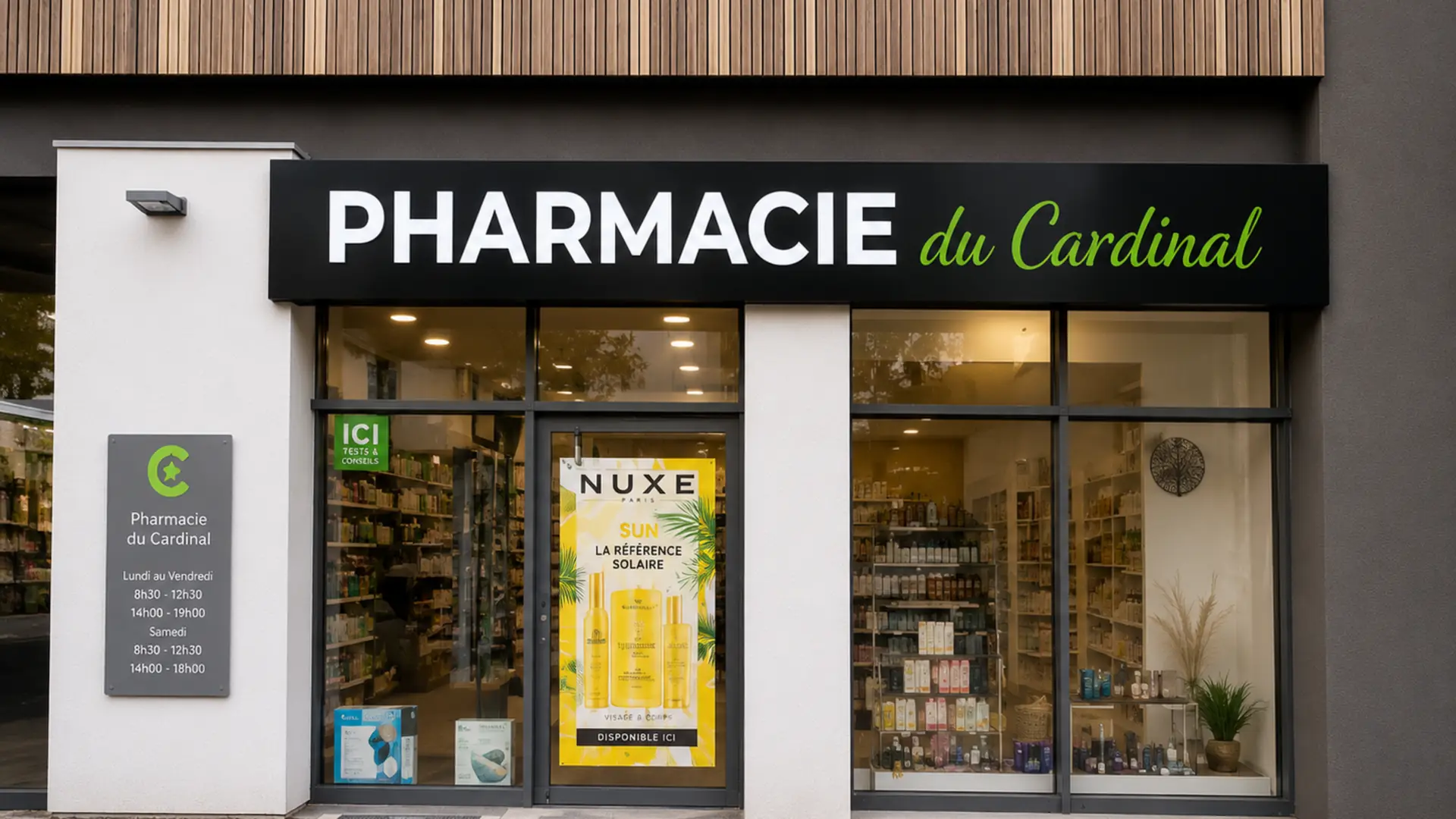 Façade de la Pharmacie du Cardinal avec vitrine, panneau horaires et affiche publicitaire Nuxe.