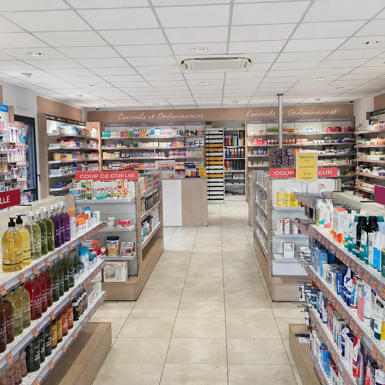 Intérieur lumineux d'une pharmacie avec rayons organisés et panneaux "Coup de cœur" visibles.