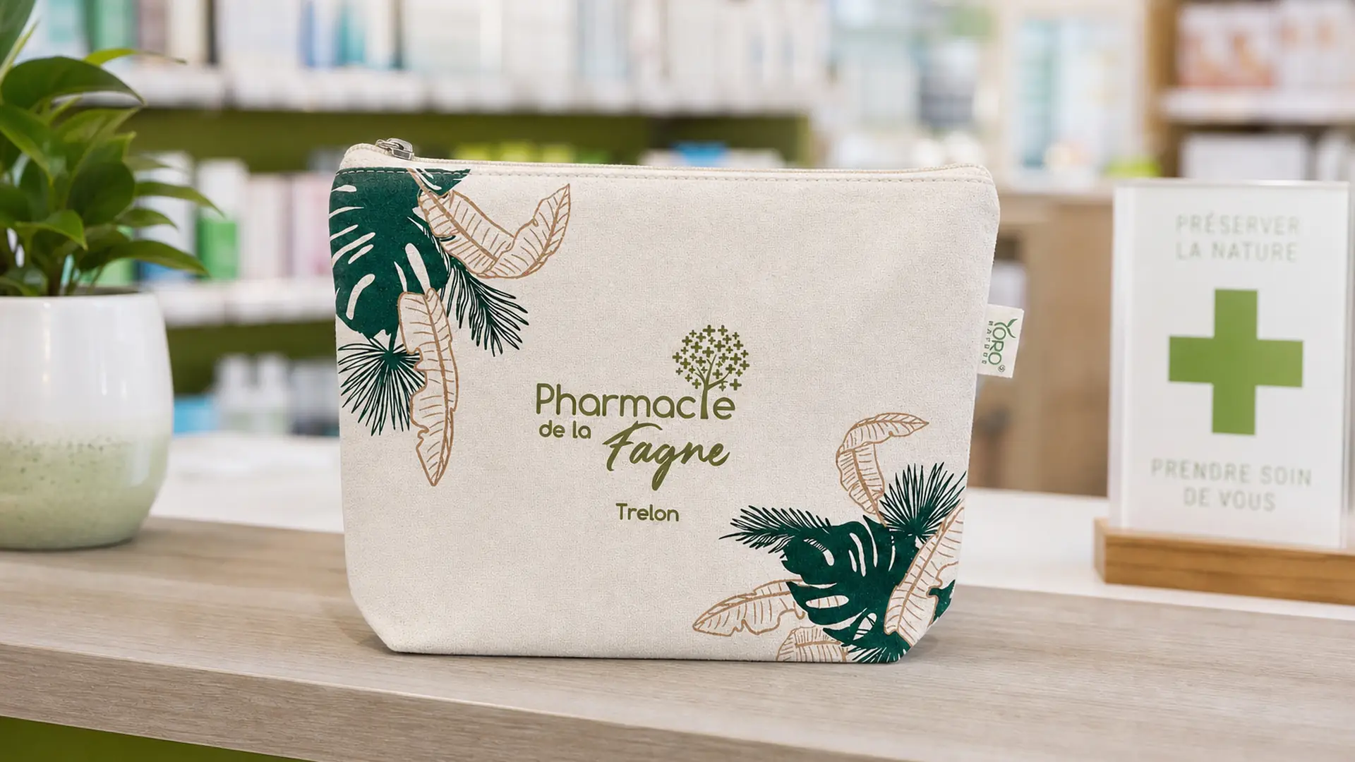 Trousse beige avec des motifs de feuilles vertes et le logo de la Pharmacie de la Fagne Trelon.
