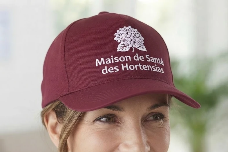 Casquette bordeaux avec logo et texte Maison de Santé des Hortensias brodés en blanc.