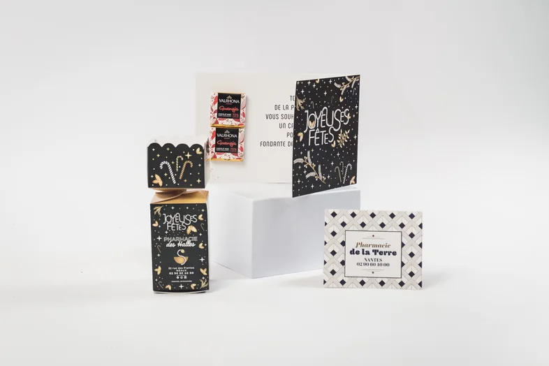 Emballages et cartes de vœux noires avec motifs dorés et texte Joyeuses Fêtes sur fond blanc.