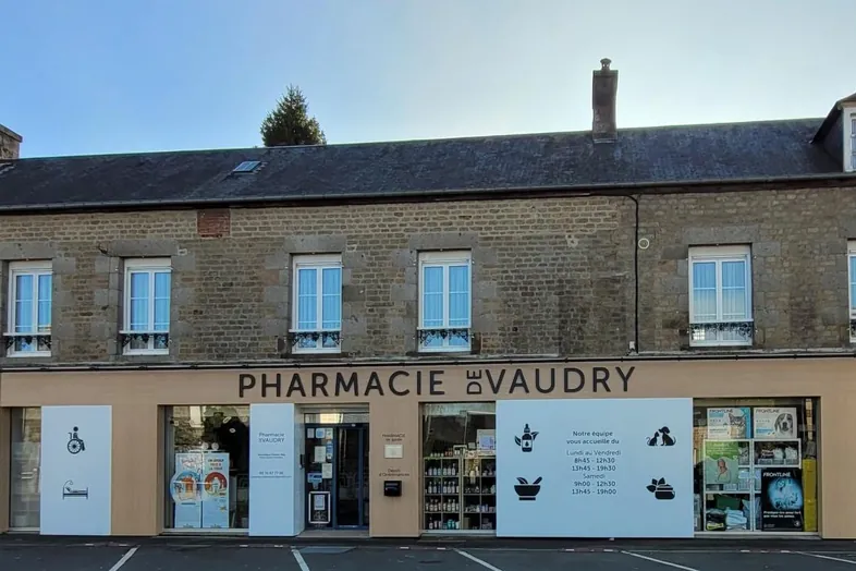 Façade d'une pharmacie en pierres avec l'enseigne PHARMACIE DE VAUDRY et vitrines illustrées.
