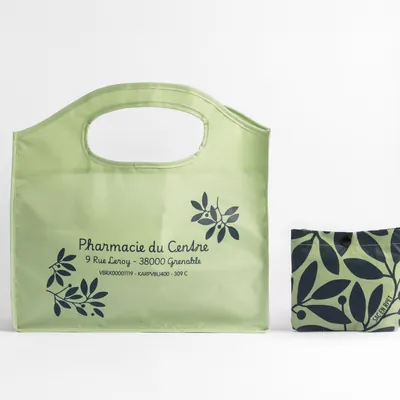 Sac pliable vert clair avec texte Pharmacie du Cendre et dessin de feuilles, à côté d'un petit sac à motifs.