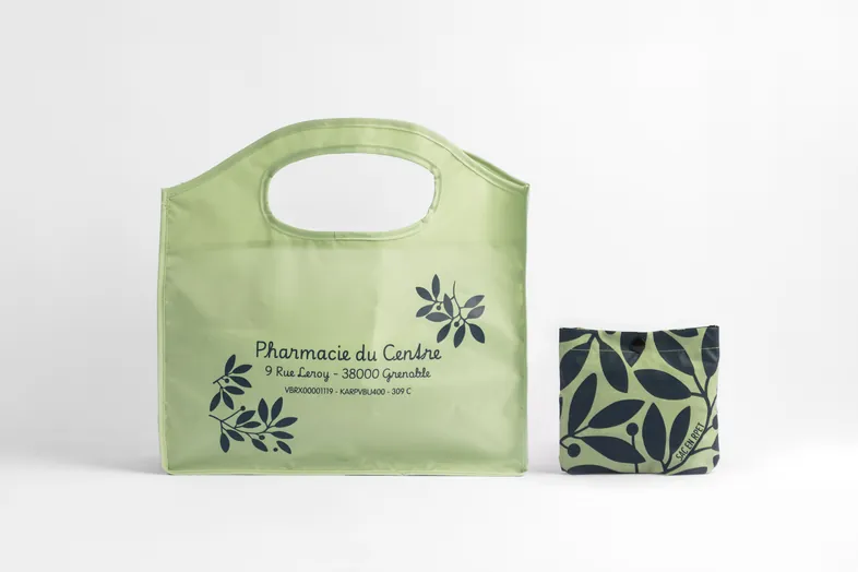 Sac pliable vert clair avec écritures noires à gauche et sac plié à motif feuilles à droite.