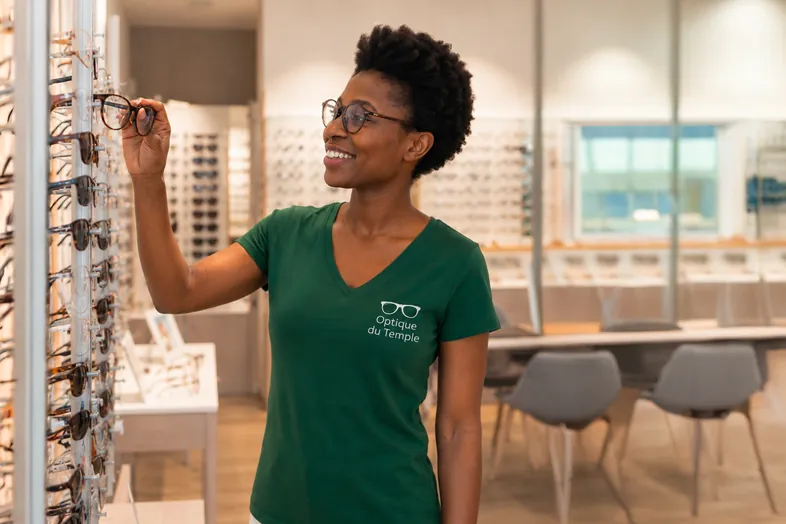 Femme souriante choisissant des lunettes dans un magasin d'optique moderne.