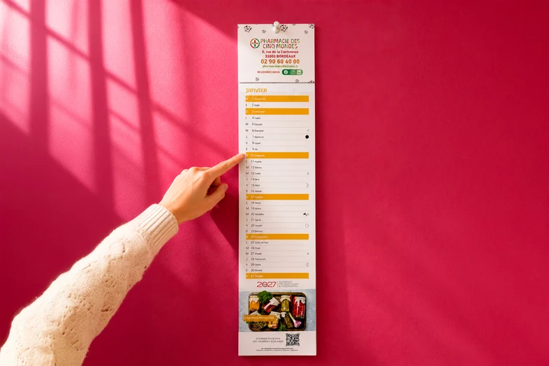 Main pointant un calendrier mural avec dates en janvier sur fond rose vif