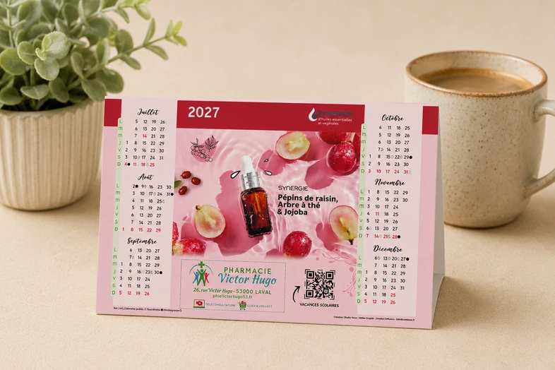 Calendrier 2027 posé sur une table avec un pot de plante et une tasse de café à côté.