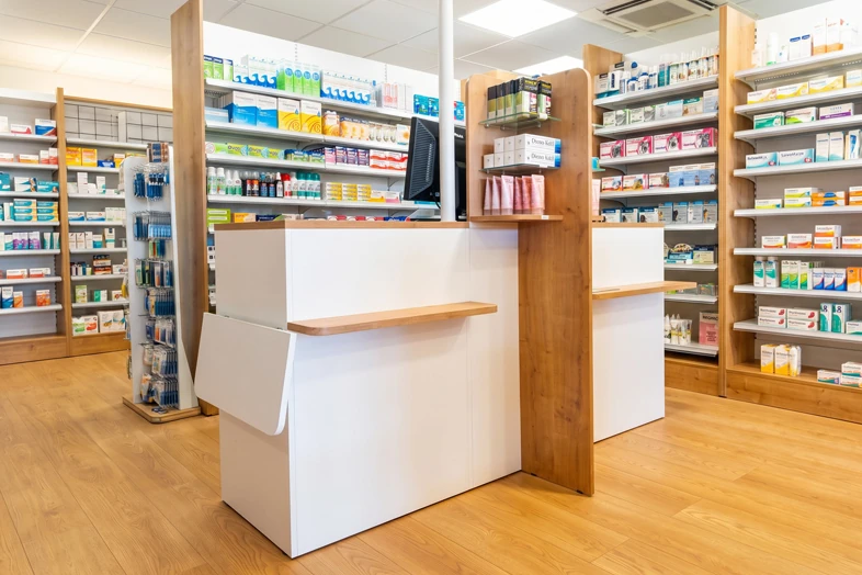 Comptoir moderne de pharmacie avec étagères en bois et produits médicaux sur fond lumineux.