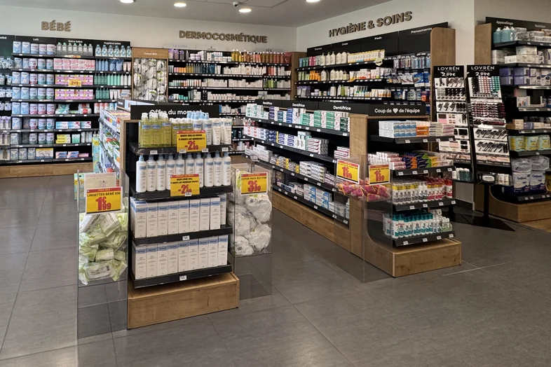 Allées de magasin avec produits bébés, dermocosmétique, et hygiène sur étagères en bois et plastique.