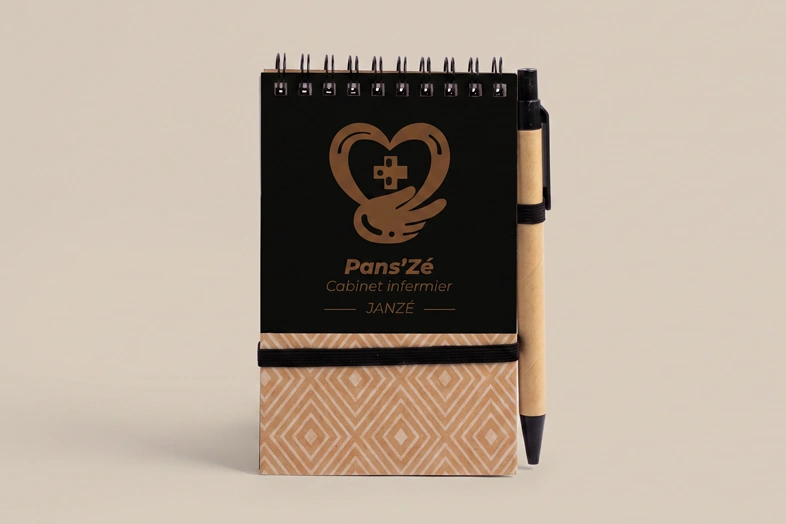 Carnet à spirale noir et kraft avec stylo, logo cœur, main et croix, texte Pans’Zé Cabinet infirmier Janzé.