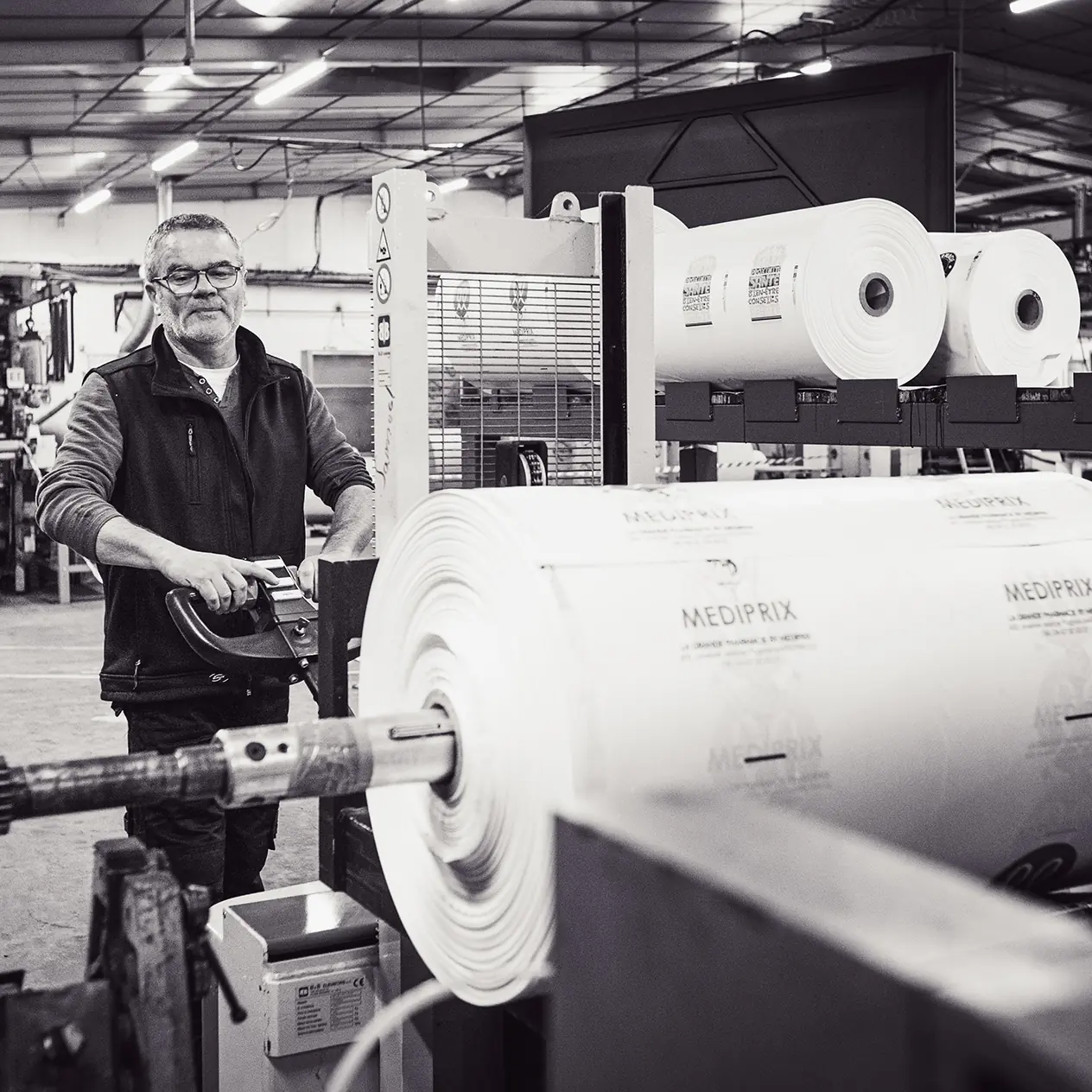 Homme dans une usine manipulant une grande bobine de matériau appelé MEDIPRIX.