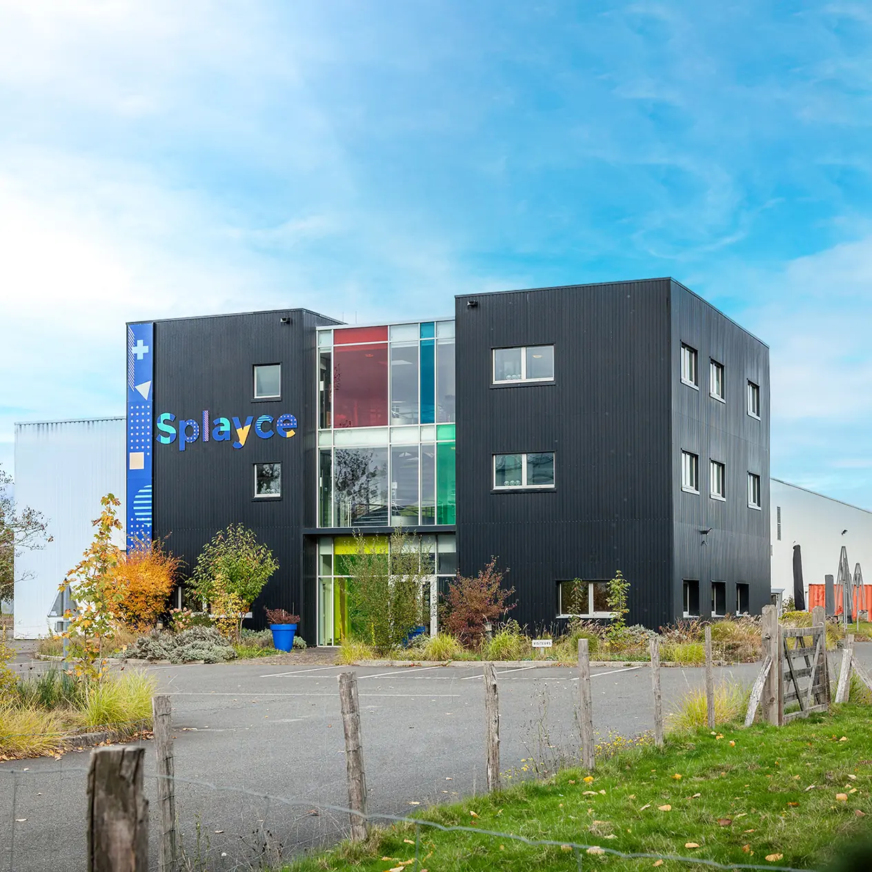 Bâtiment noir moderne à trois étages avec le logo coloré Splayce et panneaux de verre colorés.