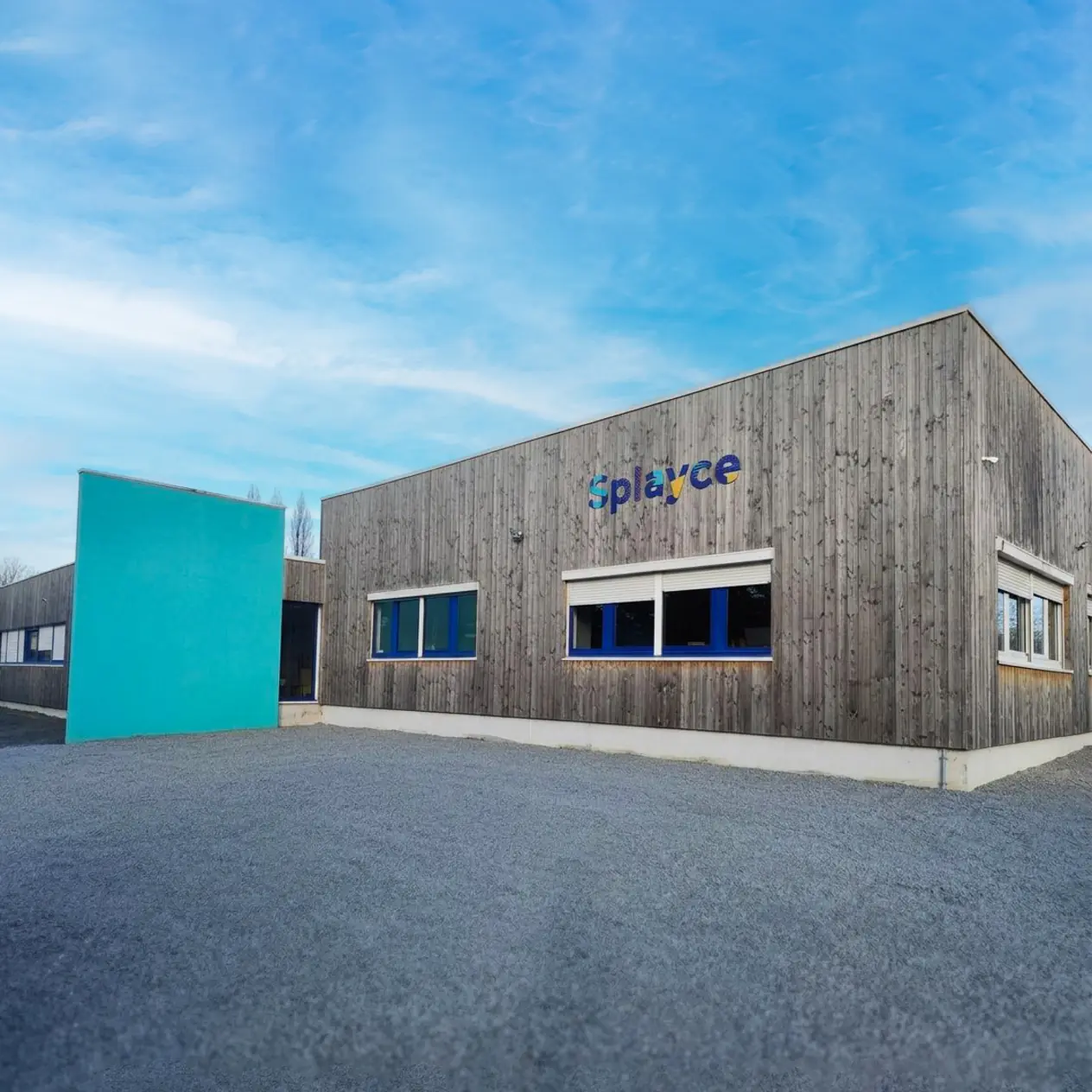 Bâtiment en bois avec le logo coloré Splayce sur le mur sous un ciel bleu clair.