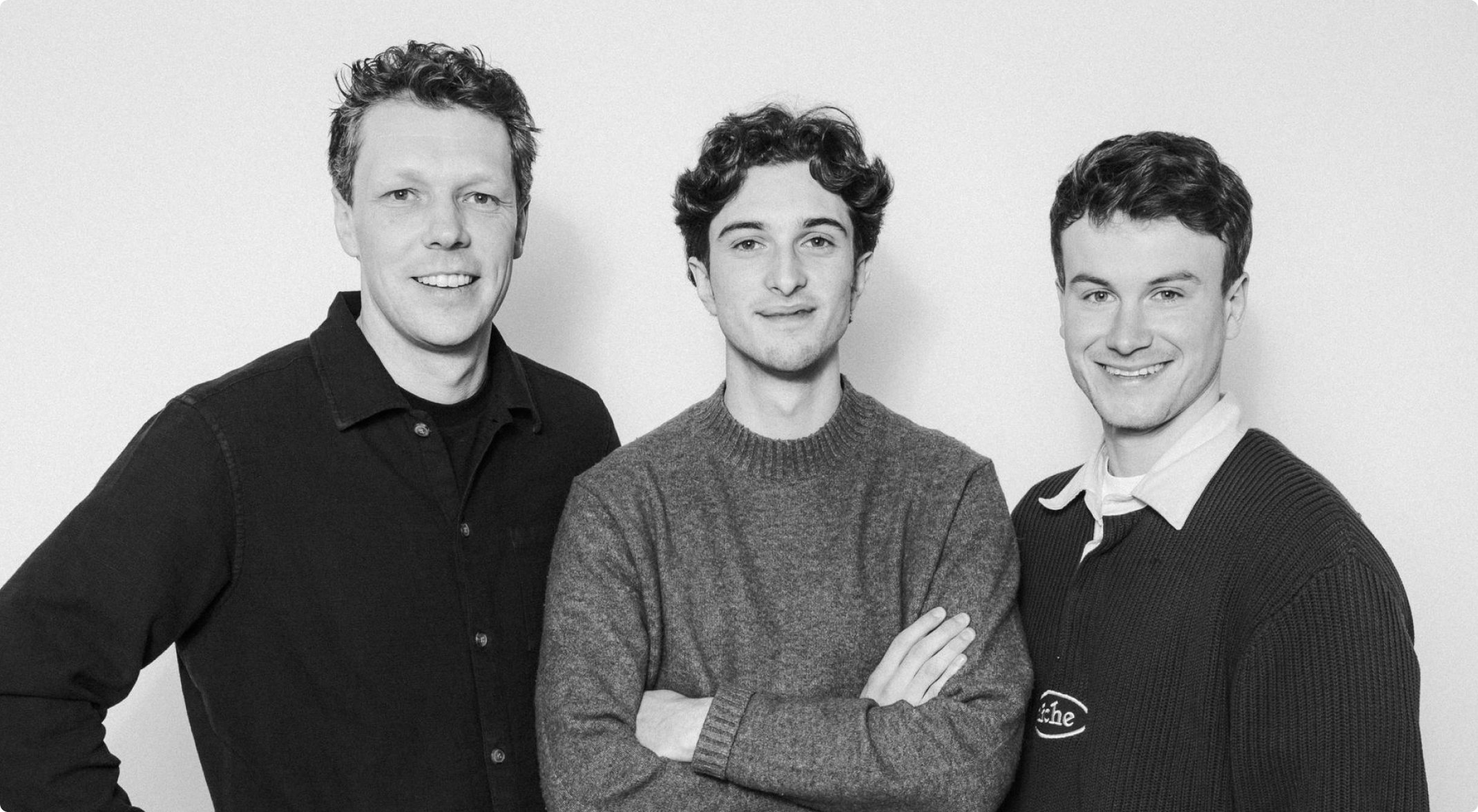 Black and white portrait of three smiling men standing side by side against a plain background.