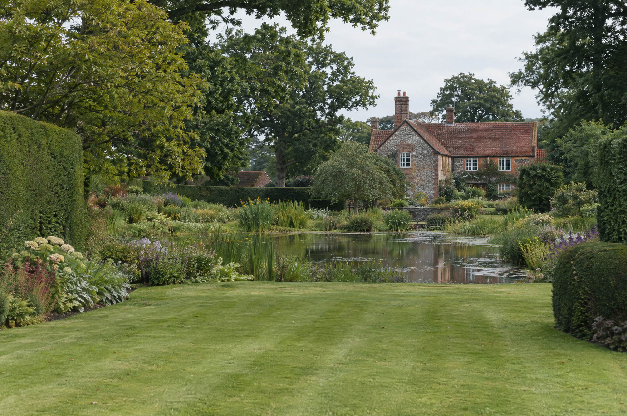 Garden pond set in the wider context of a large country garden in soft morning light