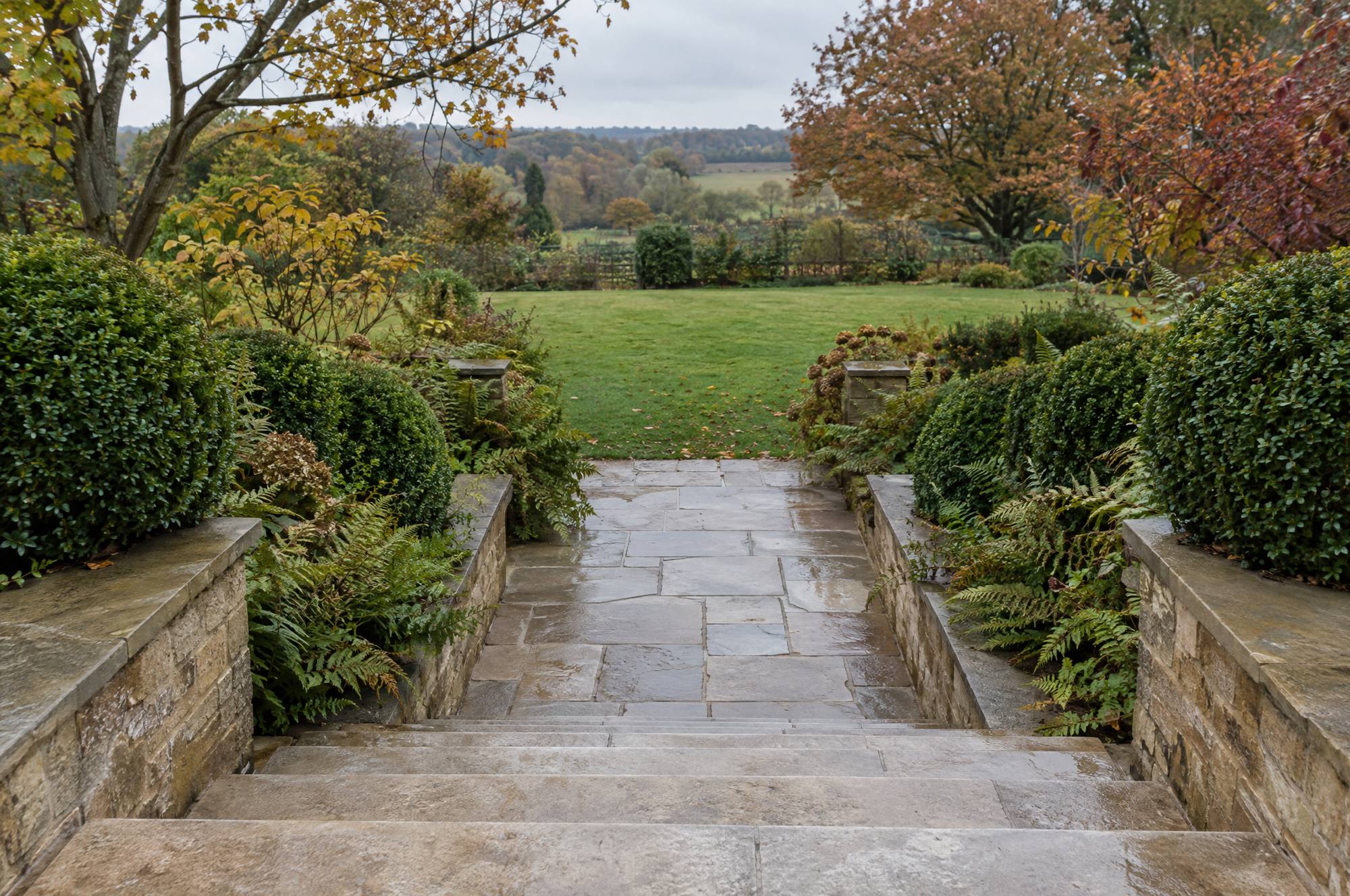 Worn York stone garden steps and flagstone path freshly cleaned of moss, descending to a lower lawn in autumn