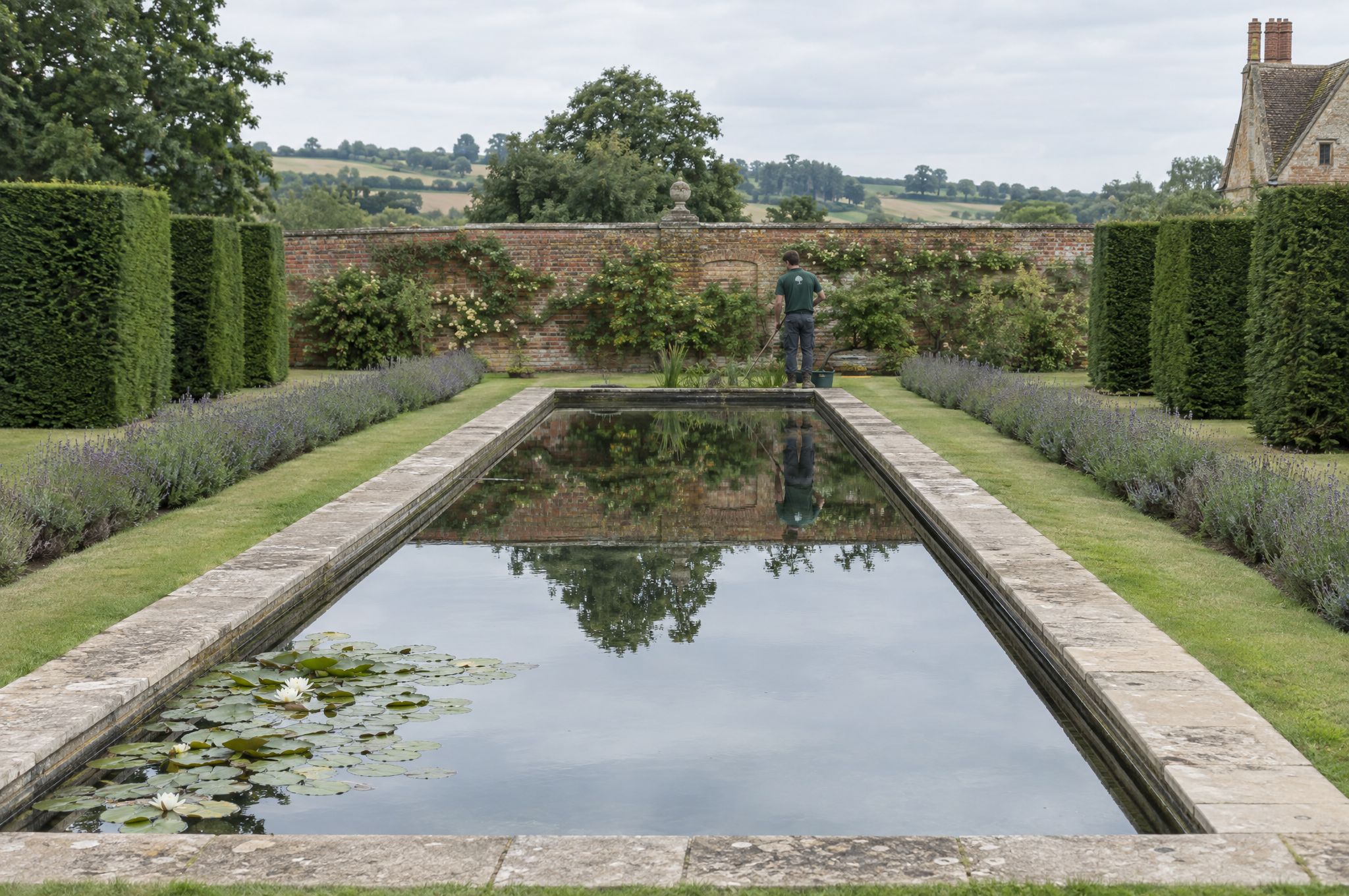 Formal rectangular reflecting pool with stone coping in a walled garden, holding a mirror reflection of the clipped yew hedges behind