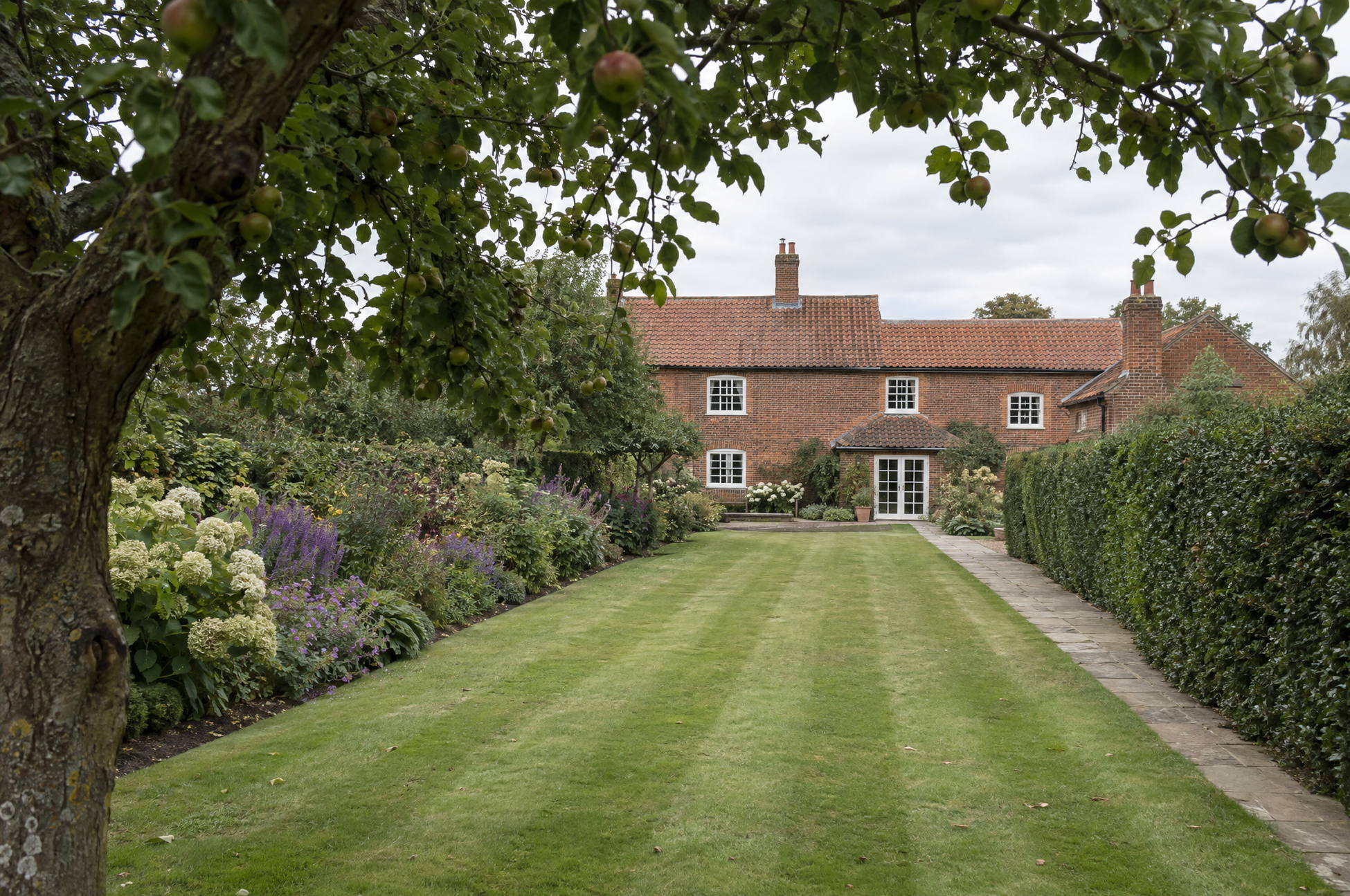 Rear garden of a red brick farmhouse reading as well looked after, with the lawn freshly cut and the bed edges clean