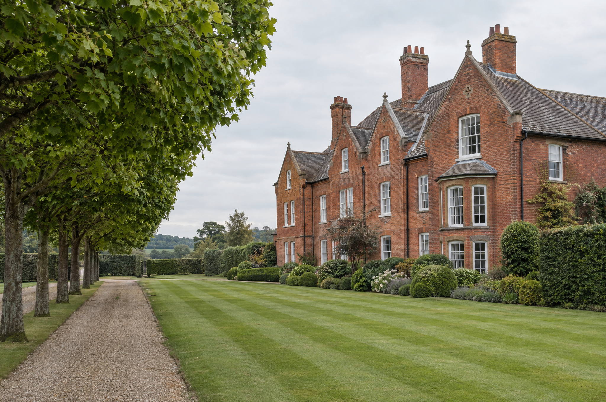 Communal grounds of a red brick country house apartment building, with mown lawns and a lime avenue along the drive