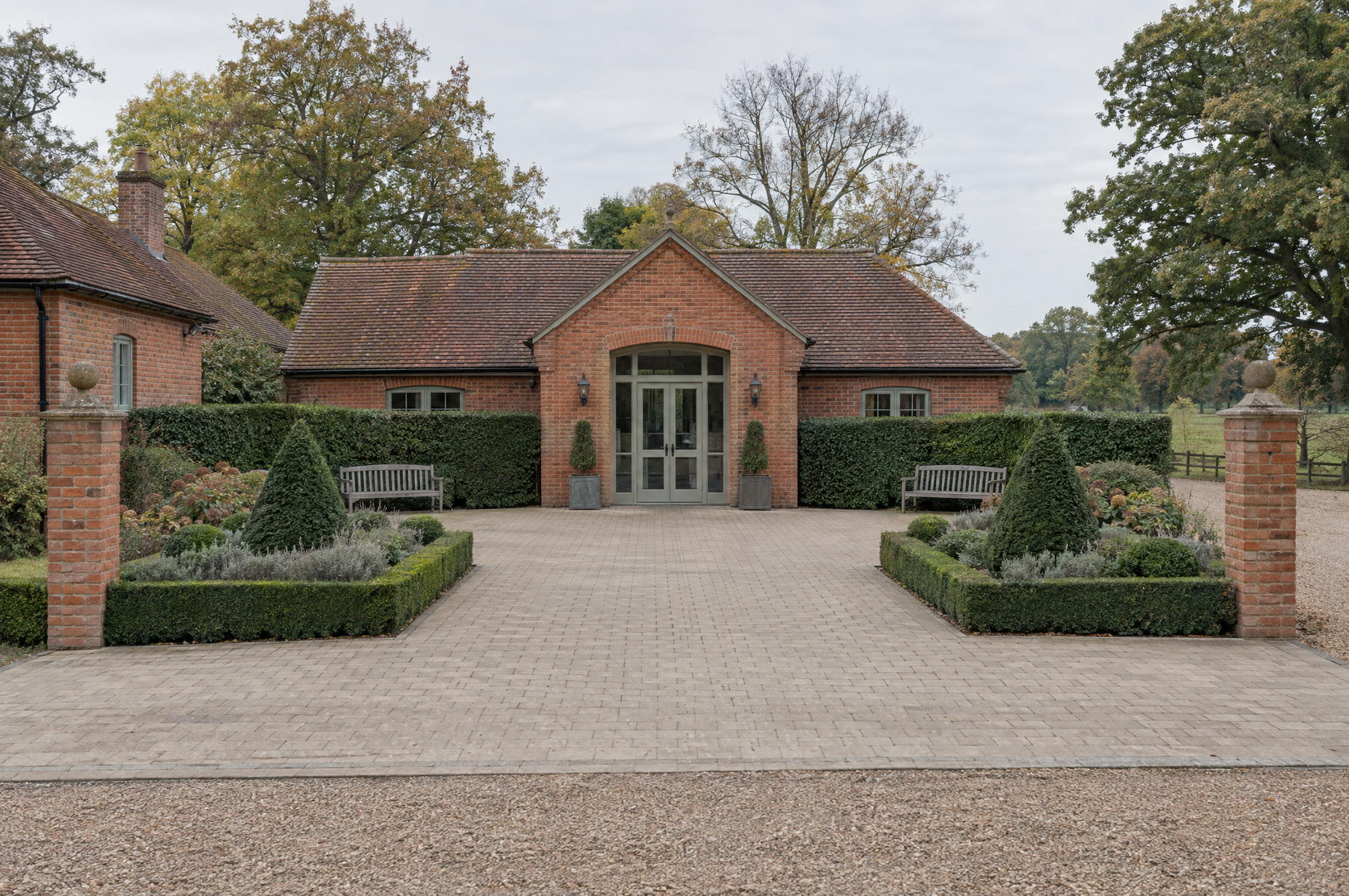 Swept entrance forecourt of a countryside office building, with formal clipped beds and timber benches